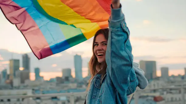 Photo of LGBT proud. Happy woman holding lgbt flag. Rooftop view