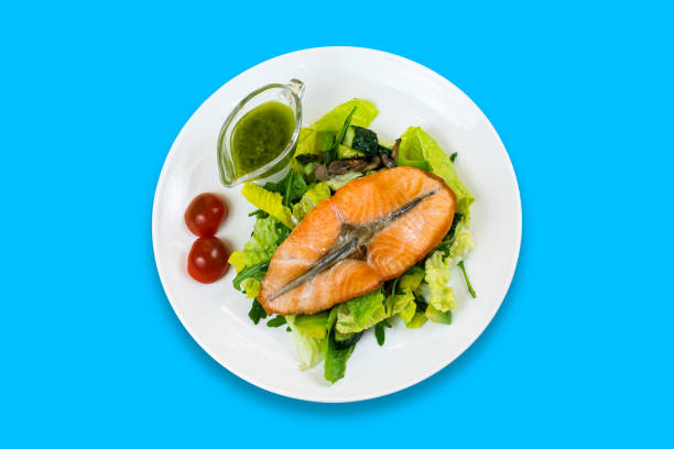 Grilled salmon steak on lettuce with cherry tomatoes and green sauce isolated on blue background