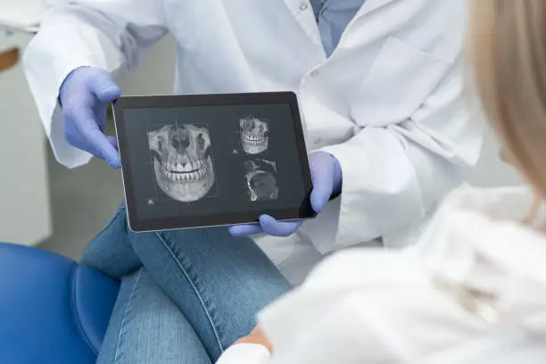 Dental consultation in clinic. Dentist showing teeth x-ray on digital tablet screen. 3D tomography technology.