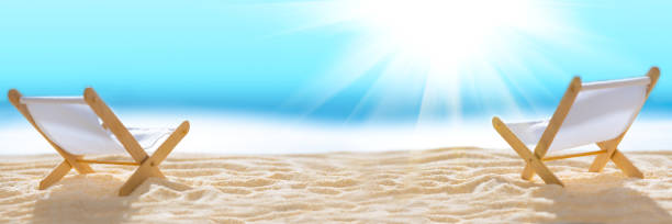 Banner 3:1. Deck chairs on sandy beach with blurry blue ocean and sun beams on sky. Social distancing or COVID-19 protection at summer holidays. Summer background. Soft focus