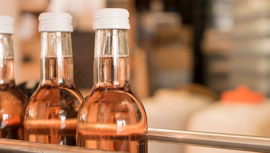 Close-up of rose wine bottles with white screw caps in an automated filling line in a german winery.