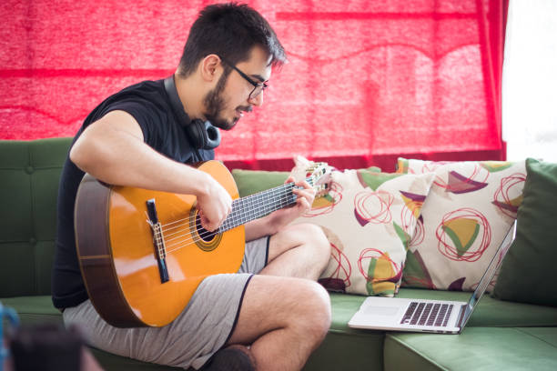 istock Young Man playing Guitar, taking online music lessons. 1231983613