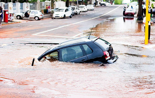Car tips into pothole in flooded street, side view  sinkhole stock pictures, royalty-free photos & images