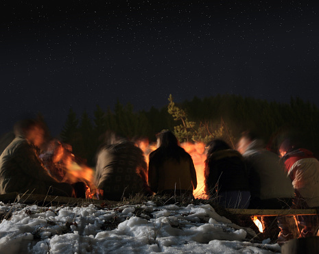 Group of young people sitting around a fireplace under the open night sky. Stars visible at higher resolutions.