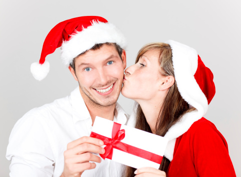 Young happy lovely kissing couple with bonus greeting card wishing a merry christmas
