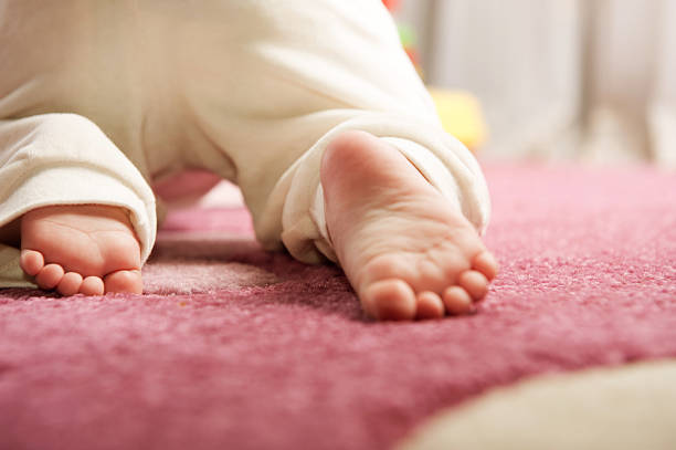 The feet of a baby crawling on a pink carpet stock photo