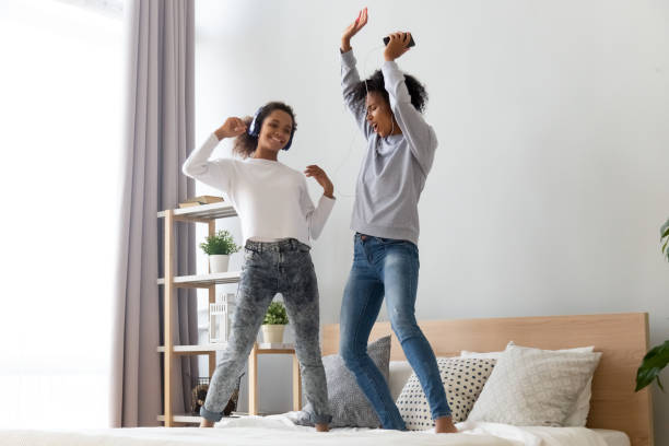 ベッドの上で踊るヘッドフォンで幸せなアフリカのお母さんと娘 - parent mother music listening ストックフォトと画像