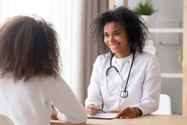 docteur africain de femme de sourire parlant au patient d’adolescent prenant des notes - serving people teenage girls female photos et images de collection