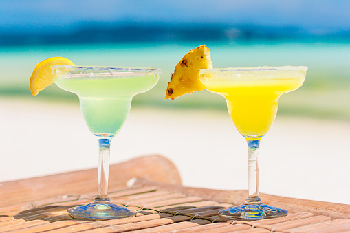 Two tasty cocktails on tropical white beach background the sea