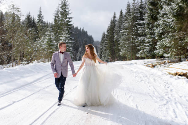 The bride and groom are walking by the hand against the backdrop of a winter forest. Snowing. stock photo