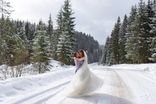 The groom circles the bride in his arms on the background of a snowy fir forest. Snowing. Winter wedding. stock photo