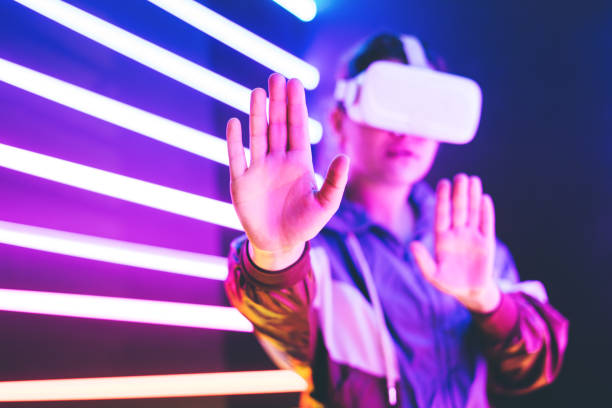 istock Girl using VR goggles in colorful neon lights studio. Put palm forward. 1232364273
