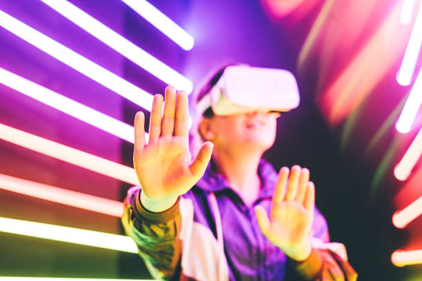 istock Girl using VR goggles in colorful neon lights studio. Put palm forward. 1232364275