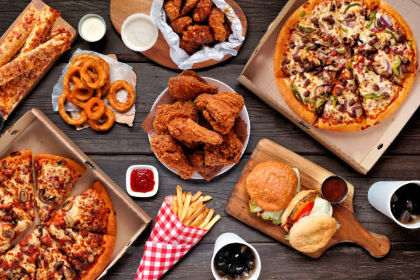 Buffet table scene of take out or delivery foods, above view over dark wood Buffet table scene of take out or delivery foods. Pizza, hamburgers, fried chicken and sides. Above view on a dark wood background. unhealthy eating stock pictures, royalty-free photos & images