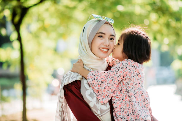 Asian young malay daughter kissing her mother cheek while smiling mother holding up her at city street Lovely family malay stock pictures, royalty-free photos & images