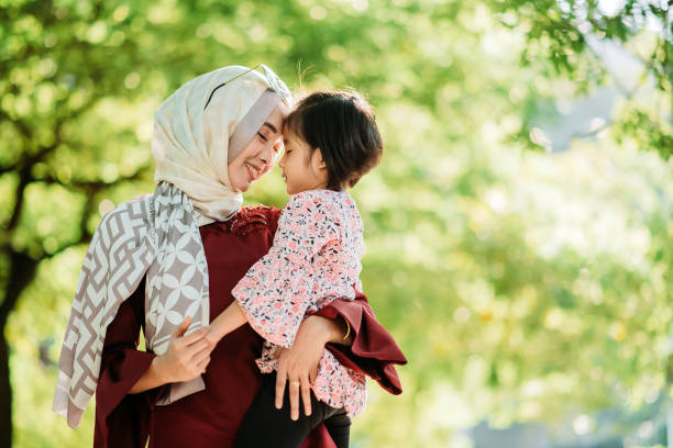 asiática joven malay sonriente madre sosteniendo a su hija y cabeza a cabeza en la calle de la ciudad - malaysian person family asian ethnicity mother fotografías e imágenes de stock