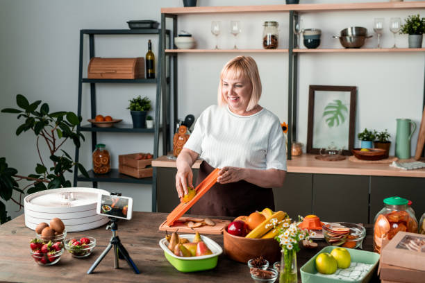 istock Happy blond middle aged female looking in smartphone camera while cooking 1232415303