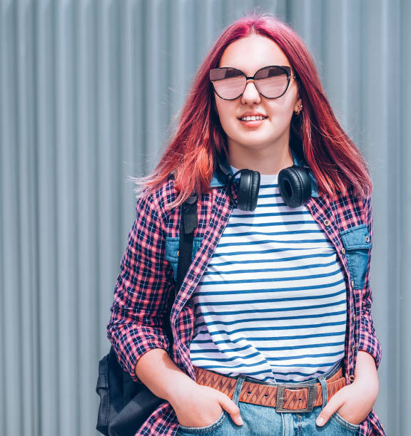 Beautiful modern smiling young female teenager with extraordinary hairstyle color in a checkered shirt and mirrored sunglasses portrait with headphones hanged on neck. Modern teens world concept image hermosa joven adolescente joven sonriente moderna con extraordinario color de peinado en una camisa a cuadros y espejo gafas de sol retrato con auriculares colgados en el cuello. imagen del concepto del mundo de los adolescentes modernos