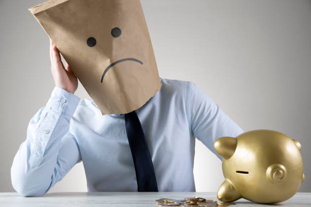 Businessman Wears Sad Face Paper Bag Piggy Bank Businessman wears a paper bag with a sad face on it The economy has pushed his business down. He is sitting in his table with piggy ban anonymous businessman with paper bag on his head stock pictures, royalty-free photos & images