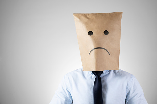 Businessman wears a paper bag with a sad face on it The economy has pushed his business down.