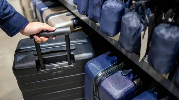 Photo of Male hand choosing suitcase luggage in the shop