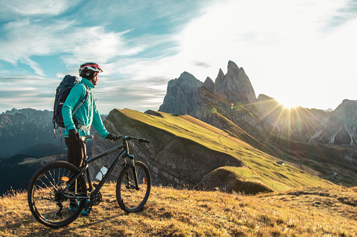 Young man with mountain bike on Seceda mountain peak at sunrise. Puez Odle, Trentino, Dolomites, Italy.