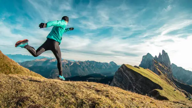 Young man in sport trail clothes running on Seceda mountain peak at sunrise. Puez Odle, Trentino, Dolomites, Italy.