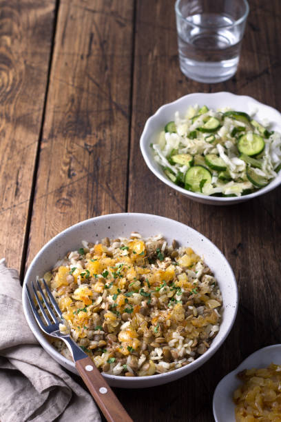 traditional middle eastern dish, mujadara of lentils, rice and fried onions with a salad of cabbage and cucumbers on wooden table - cooked vertical high angle view lentil imagens e fotografias de stock