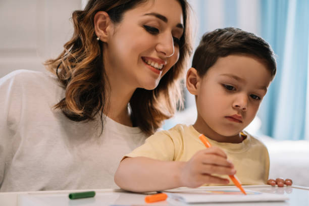 istock cheerful mother looking at adorable son drawing with felt-tip pen 1232598391