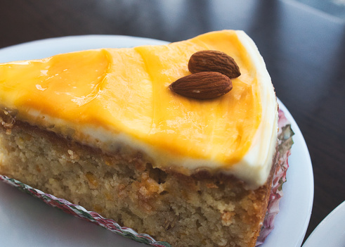 Close-up of a slice of carrot cake with orange icing and almonds on top