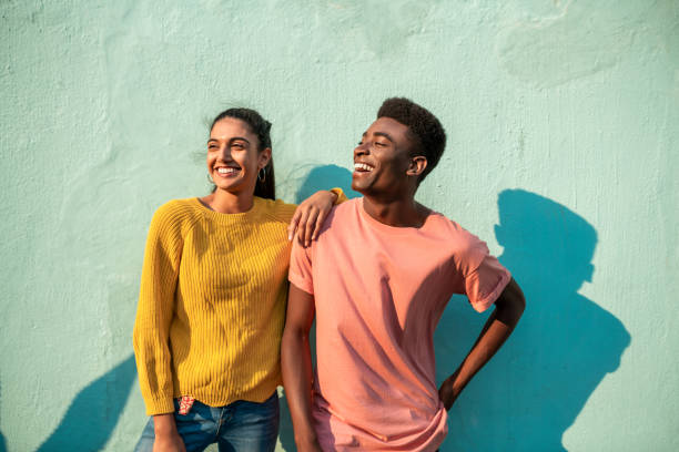 Portrait of two smiling couple looking away. Portrait of Young couple. They are looking away laughing and leaning on light blue wall friendship stock pictures, royalty-free photos & images