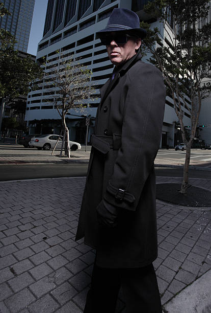 Portrait of a stylish young adult wearing sunglasses and a black leather jacket with a scarf. He is photographed standing on a metal fire escape by the side of a building.