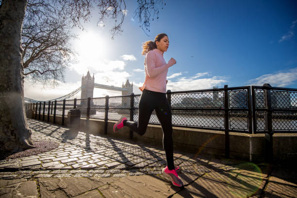 young woman running alone by the river thames - london england morning sunlight tower bridge imagens e fotografias de stock