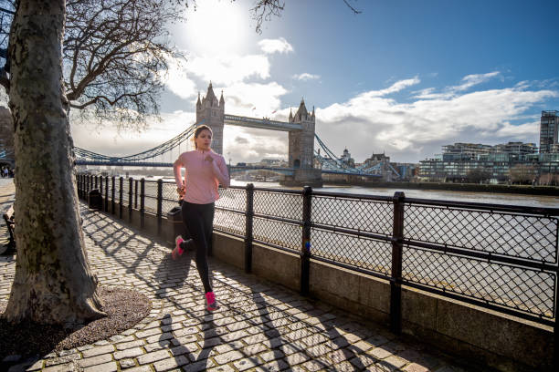 Young woman jogging alone by the river Thames Young woman in sports clothes jogging alone down the walkway by the river Thames at time of Covid-19 isolation tower bridge london england bridge europe stock pictures, royalty-free photos & images