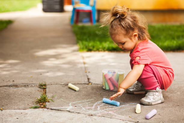 Fun with chalks for a girl in her back yard Low angle view of cute little girl crouching down to paint a drawing with chalk on the concrete floor of the yard in her house. toddler stock pictures, royalty-free photos & images