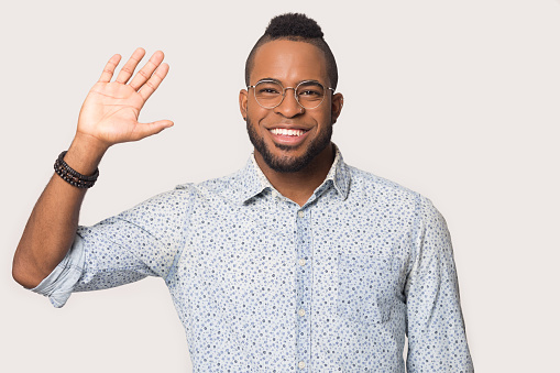 Head shot portrait handsome African American man in glasses looking at camera, happy student waving hand in greeting gesture, giving high five to friend, isolated on white studio background