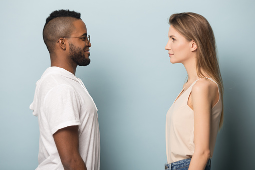 African American man in glasses and beautiful Caucasian woman looking at each other eyes to eyes, sideways view, diverse couple in love, support and care, isolated on studio background