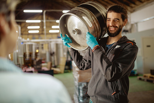 Worker carrying beer barrel on shoulder and smiling at manager