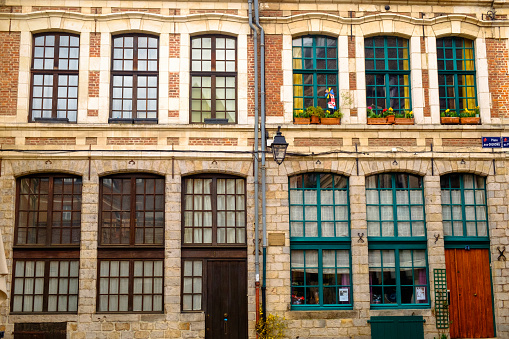 Two symmetrical historic houses stand next to each other in the old town of Lille. The high windows have either green or brown muntins.