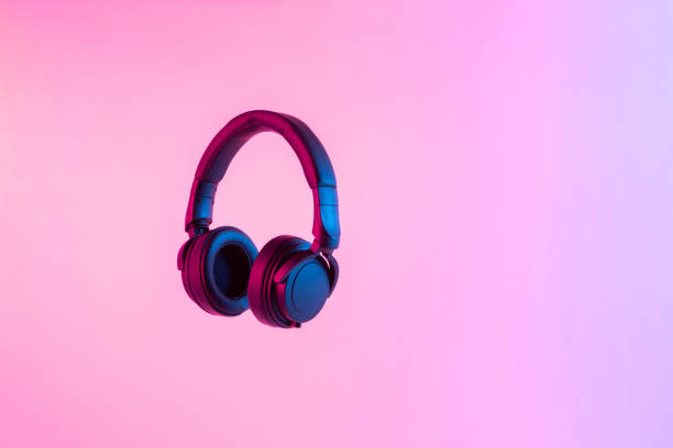 futuristic concept with stylish black wireless headphones lit with colorful neon light isolated on abstract background with empty space - brightly lit audio imagens e fotografias de stock