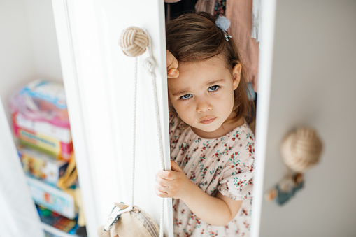 Little girl looking out of wooden open door wardrobe