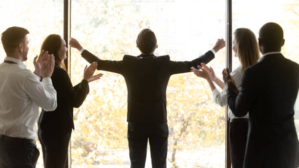 Businesspeople applauding admired by talent and success of colleague Rear view happy team leader stands near window in office raised his hands feel excited about business win. Corporate staff applauding showing respect admired by talent and success of colleague concept admired stock pictures, royalty-free photos & images