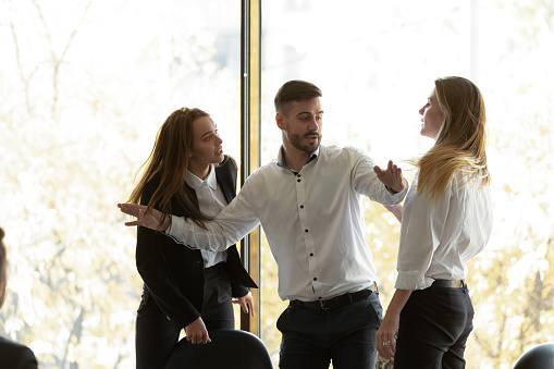 Two businesswomen having conflict at group meeting in boardroom, standing starting fight showing negative attitude colleague try to stop scuffle, confrontation, struggle for leadership at work concept