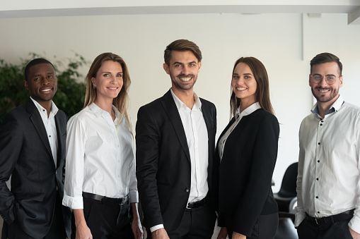 Five attractive good-looking multi-ethnic millennial professionals posing at workplace standing in row smiling looking at camera feeling self-confidence. Successful corporate group portrait concept