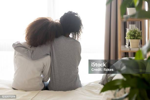 Loving African Single Mother Embrace Teen Daughter Sit On Bed Stock Photo - Download Image Now