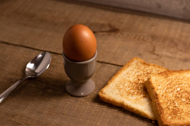 istock Boiled egg in an egg cup with a slice of fried toast bread and a spoon on a natural brown wooden background. 1233195085
