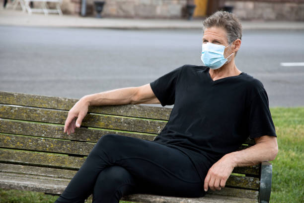 istock Man wearing surgical mask sitting on park bench relaxing 1233368261