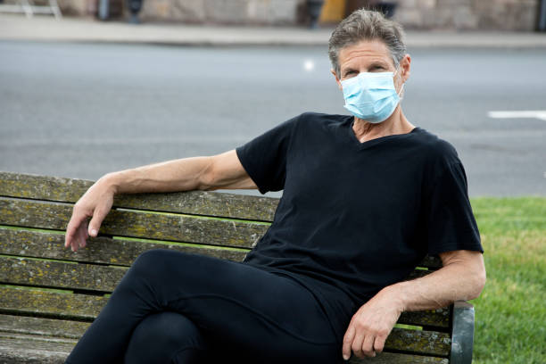 istock Man wearing surgical mask sitting on park bench looking at camera 1233368773