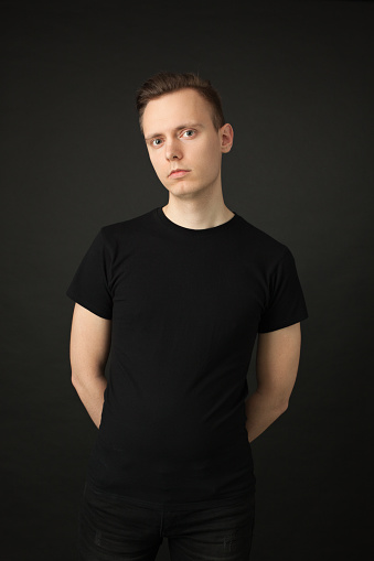 studio portrait of a 24 year old man with brown hair in a black t-shirt and black jeans on a black background
