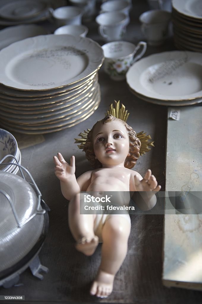 Baby Jesus statuette relegated to an antiques store Catholic baby Jesus statuette with a golden halo and outstretched arms lying amongst bric-a-brac in an antiques or thrift store.  The thrift store location could represent religion (catholicism/ christianity) being relegated to the past or the rediscovery of religion. Antique Stock Photo